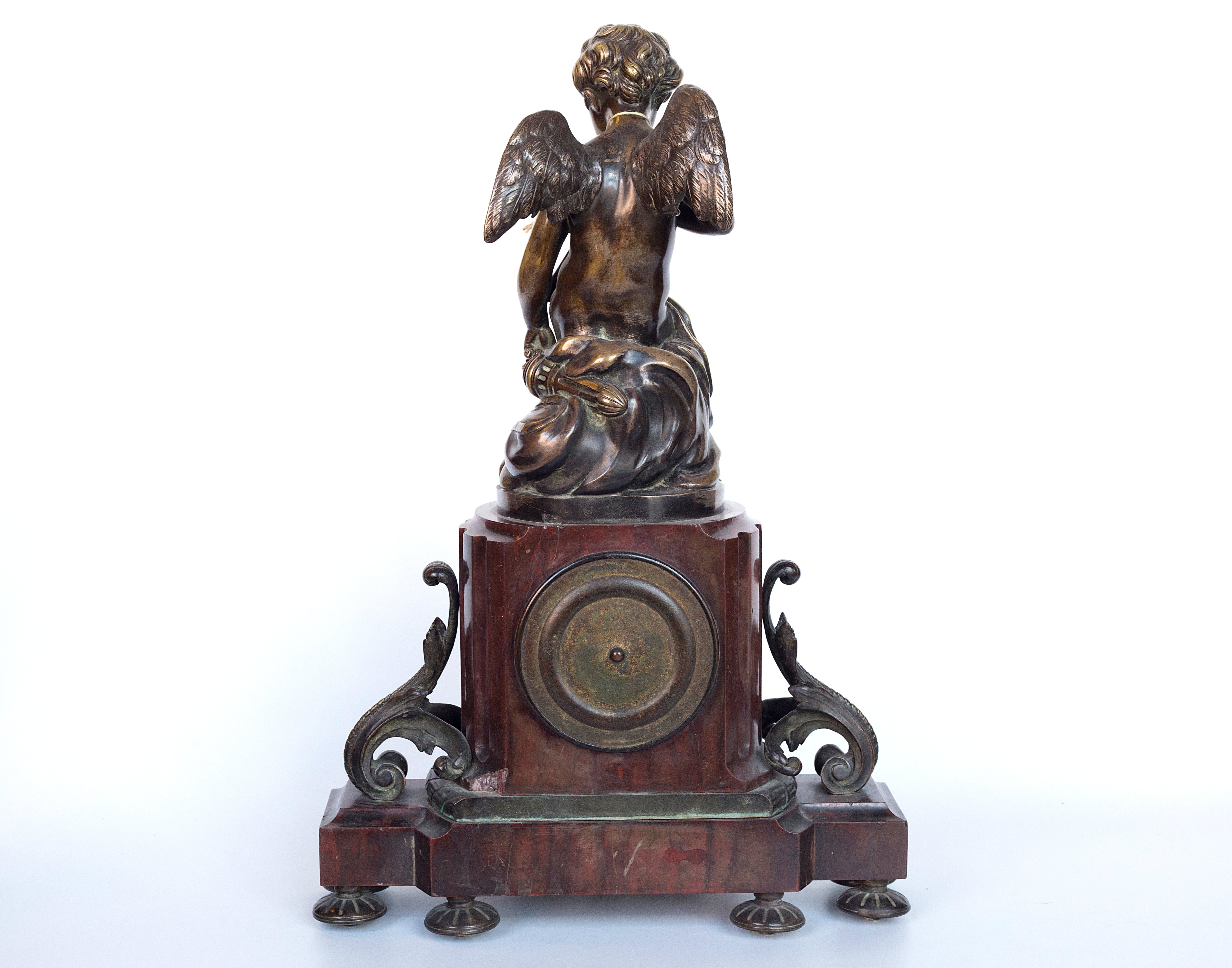 Antique handcrafted bronze clock sits atop a stone plinth, featuring a sculpture of a Putti, inspired by the French Rococo sculptor Clodion (Claude Michel)