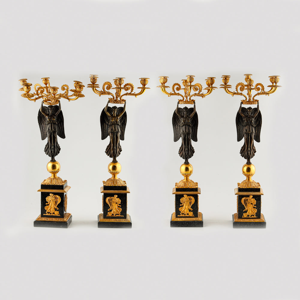 A collection of four gilt bronze candelabras adorned with bronze winged Victory sculptures