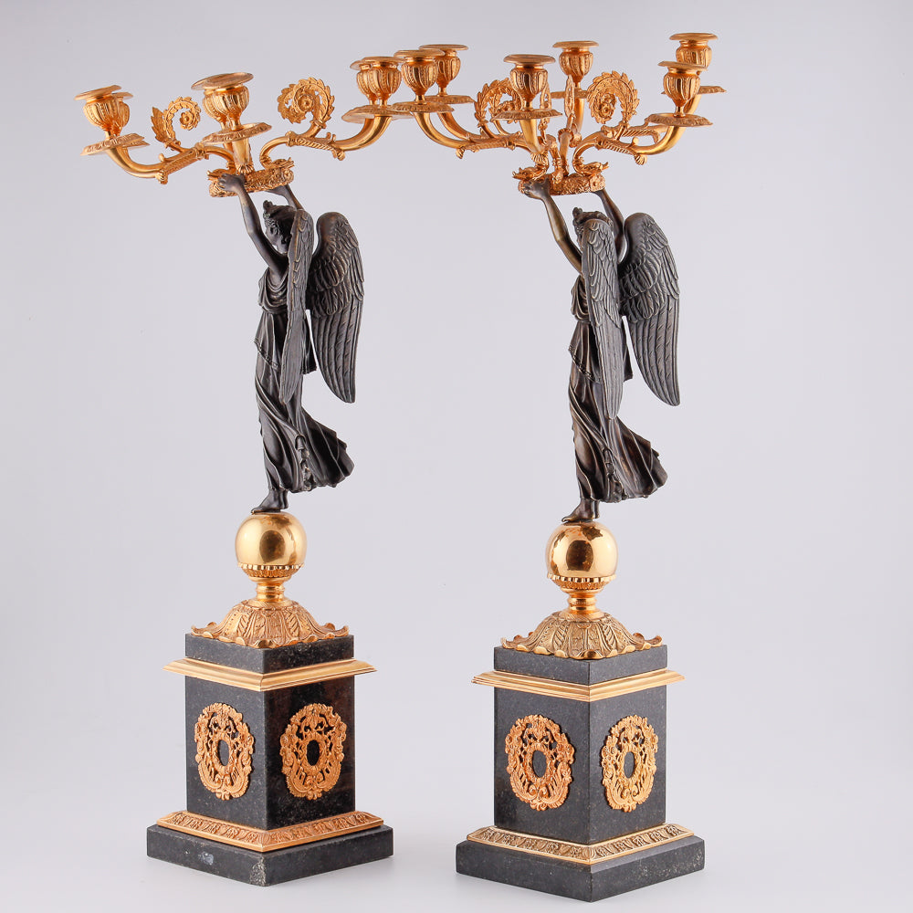 A collection of four gilt bronze candelabras adorned with bronze winged Victory sculptures