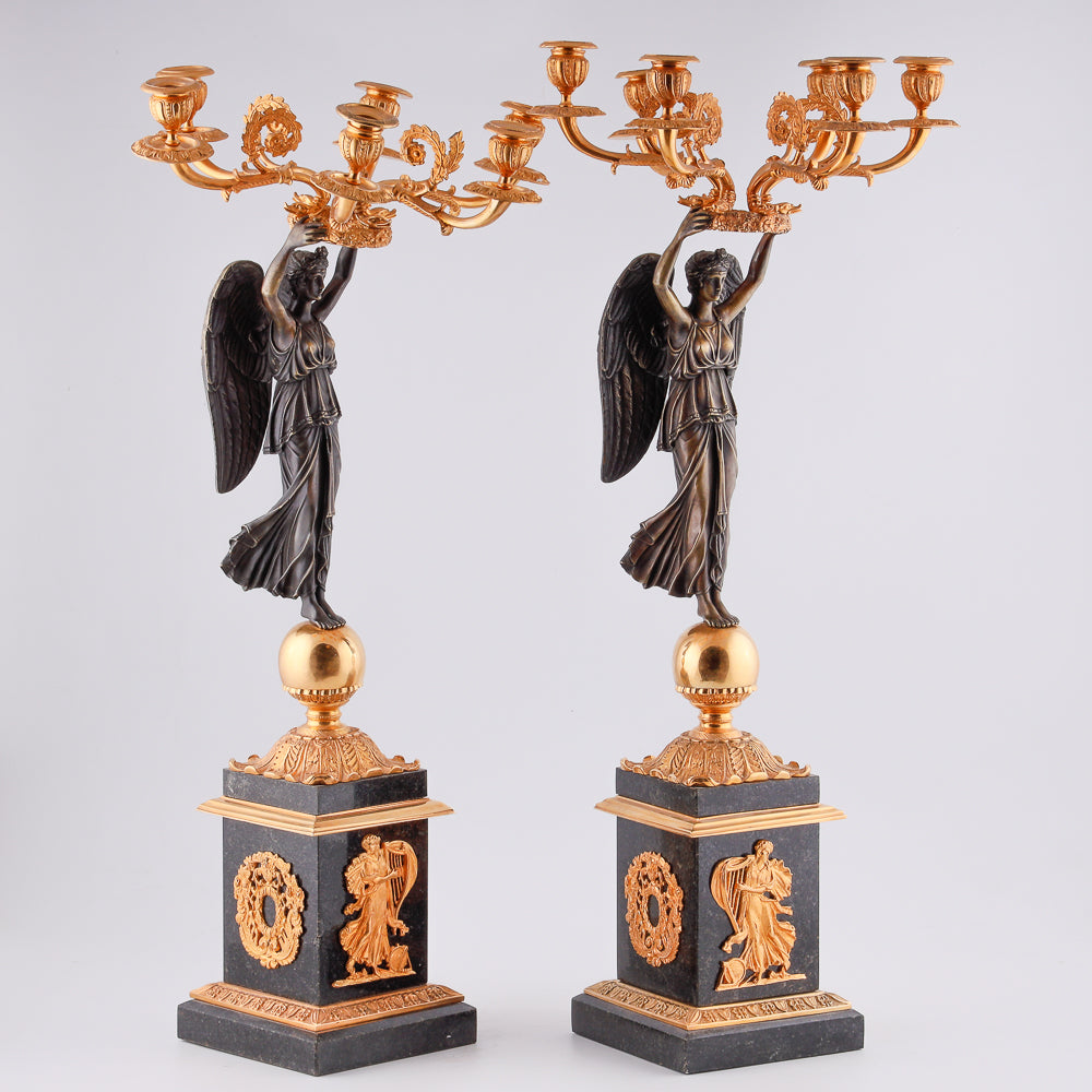 A collection of four gilt bronze candelabras adorned with bronze winged Victory sculptures