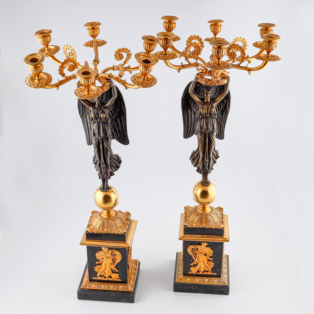 A collection of four gilt bronze candelabras adorned with bronze winged Victory sculptures