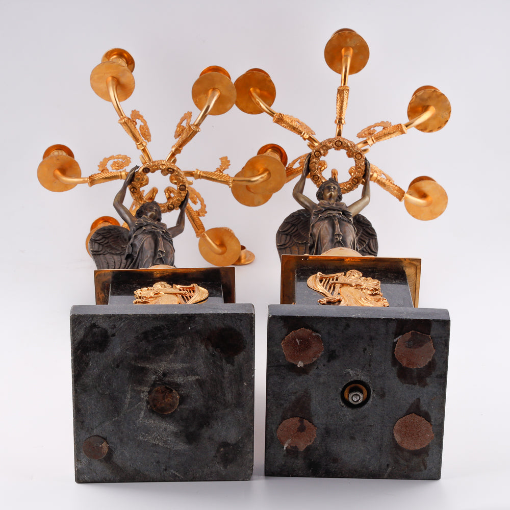 A collection of four gilt bronze candelabras adorned with bronze winged Victory sculptures