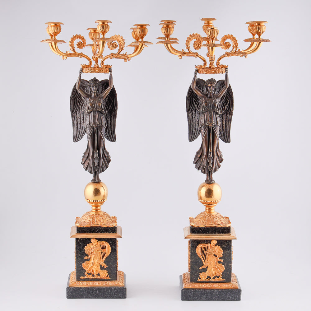 A collection of four gilt bronze candelabras adorned with bronze winged Victory sculptures