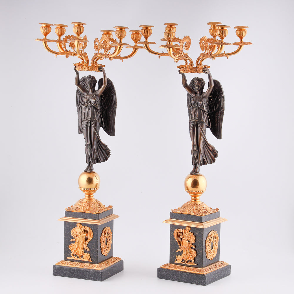 A collection of four gilt bronze candelabras adorned with bronze winged Victory sculptures