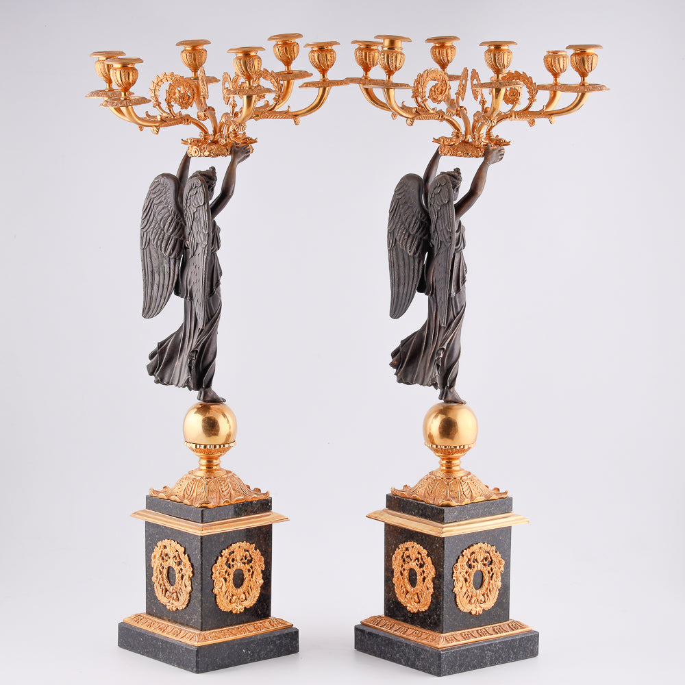 A collection of four gilt bronze candelabras adorned with bronze winged Victory sculptures
