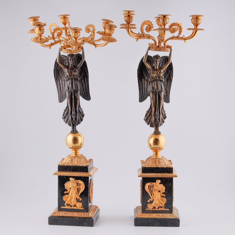 A collection of four gilt bronze candelabras adorned with bronze winged Victory sculptures