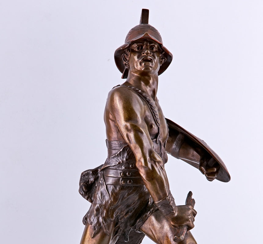 A bronze sculpture by Edouard Drouot, dating from the late 19th century, captures the dramatic moment between a gladiator and a defeated lion
