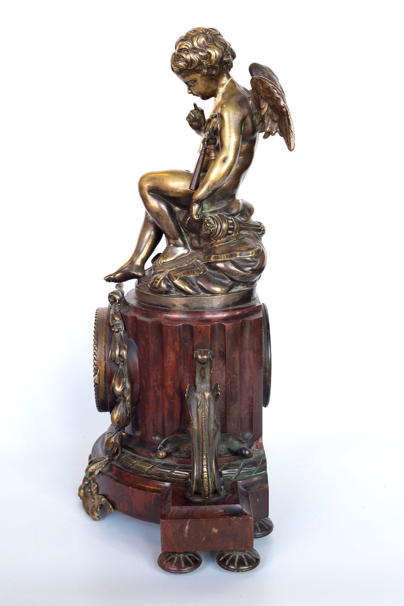 Antique handcrafted bronze clock sits atop a stone plinth, featuring a sculpture of a Putti, inspired by the French Rococo sculptor Clodion (Claude Michel)