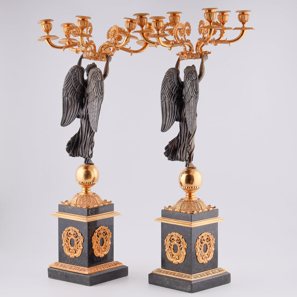 Cuatro candelabros antiguos con una estatua de la victoria alada.