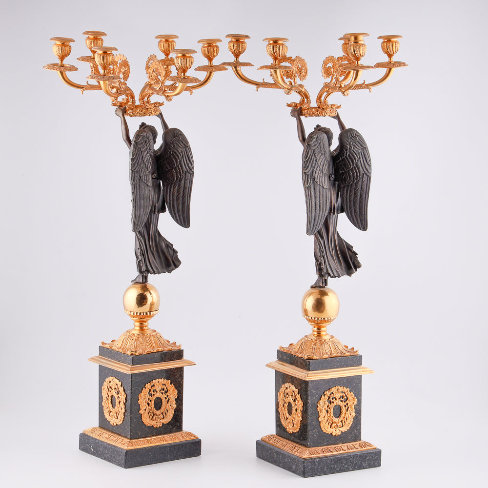 Cuatro candelabros antiguos con una estatua de la victoria alada.