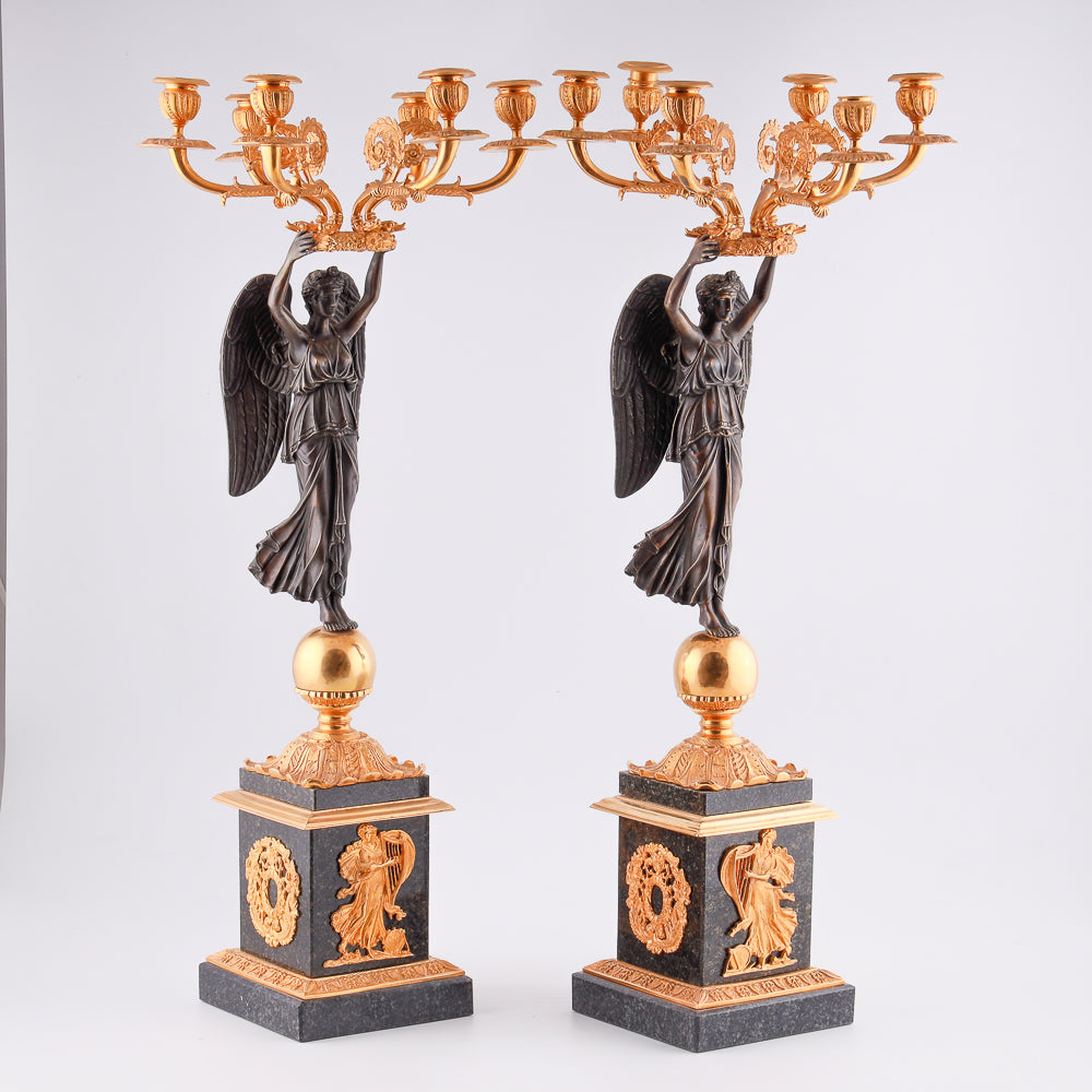 Cuatro candelabros antiguos con una estatua de la victoria alada.