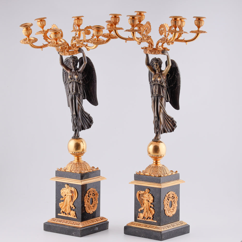 Cuatro candelabros antiguos con una estatua de la victoria alada.