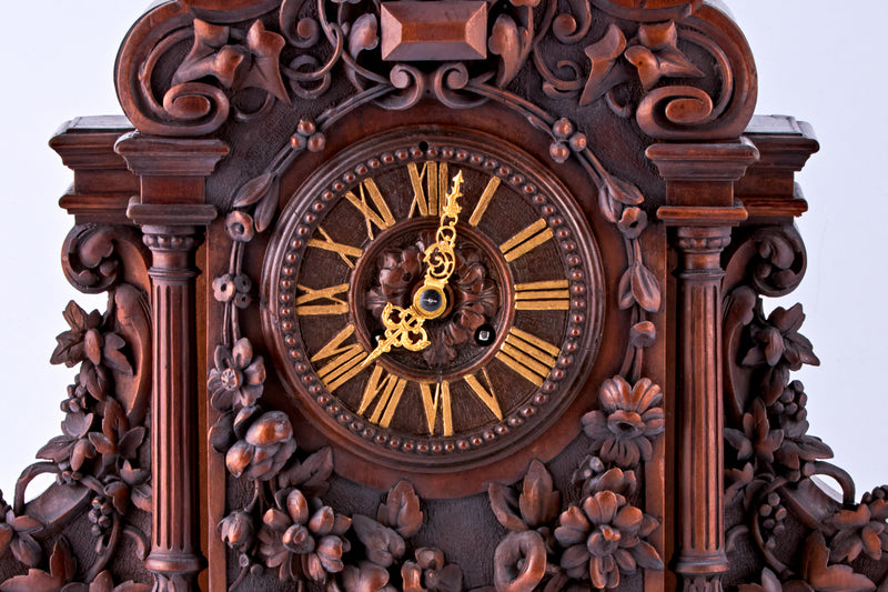 Reloj de nogal tallado a mano con números romanos en la esfera y decorado con motivos florales tallados