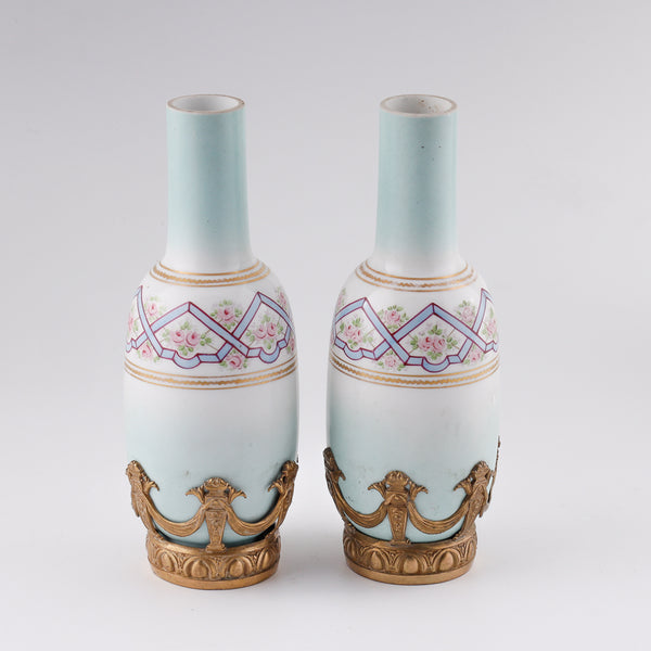 Antiguo par de pequeños jarrones decorativos franceses de porcelana en un entorno de bronce dorado.