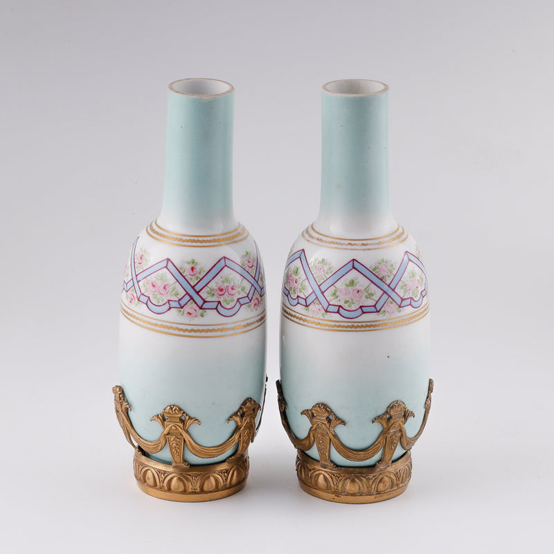 Antiguo par de pequeños jarrones decorativos franceses de porcelana en un entorno de bronce dorado.