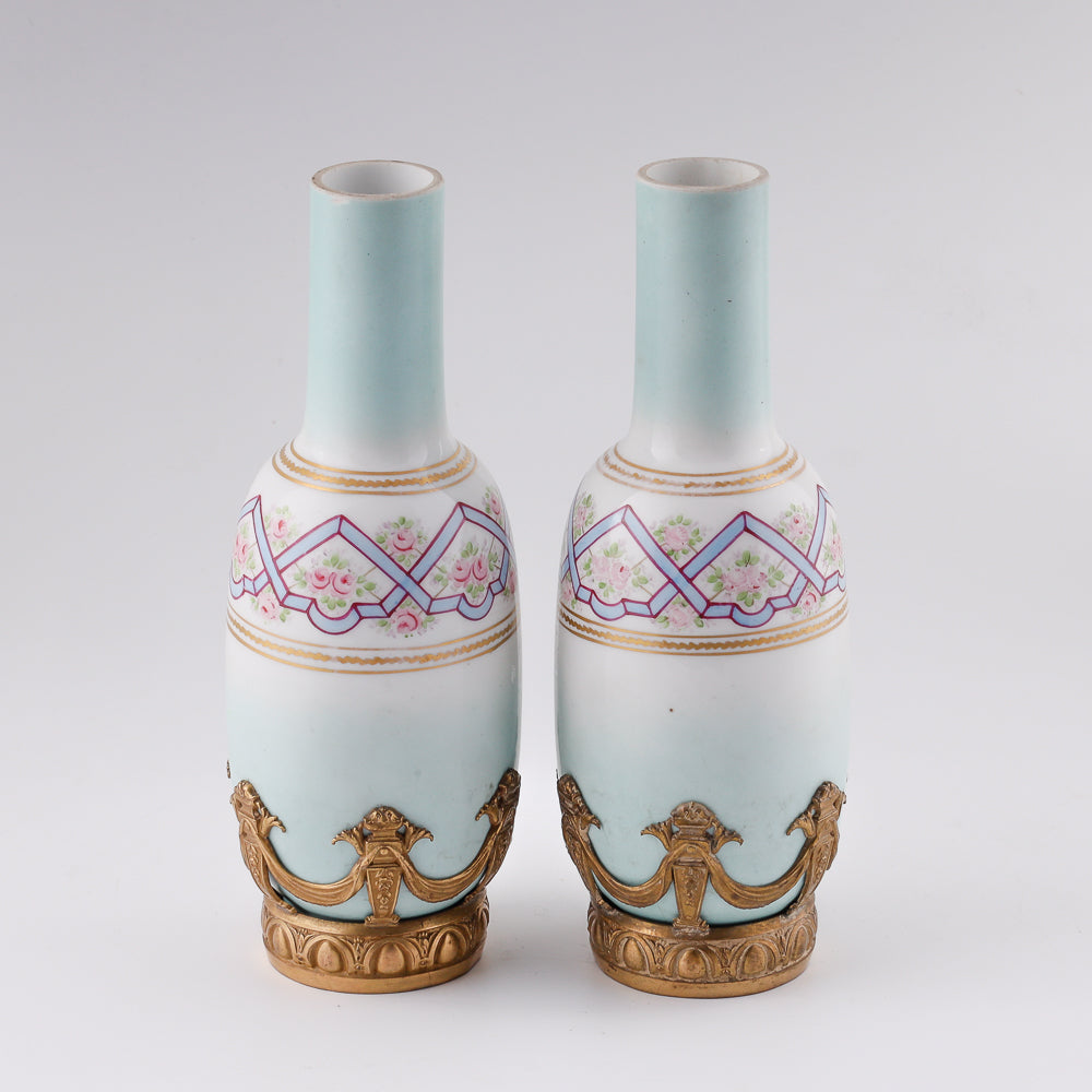 Antiguo par de pequeños jarrones decorativos franceses de porcelana en un entorno de bronce dorado.