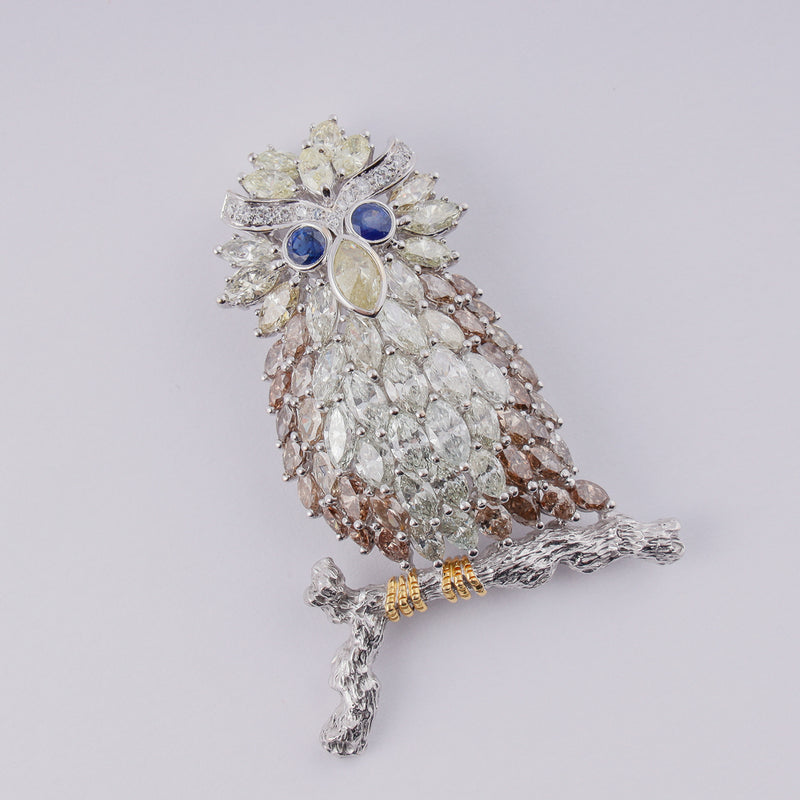 18k white gold brooch designed as an owl on a branch set with 14,18 CTW of diamonds and 2 blue sapphires